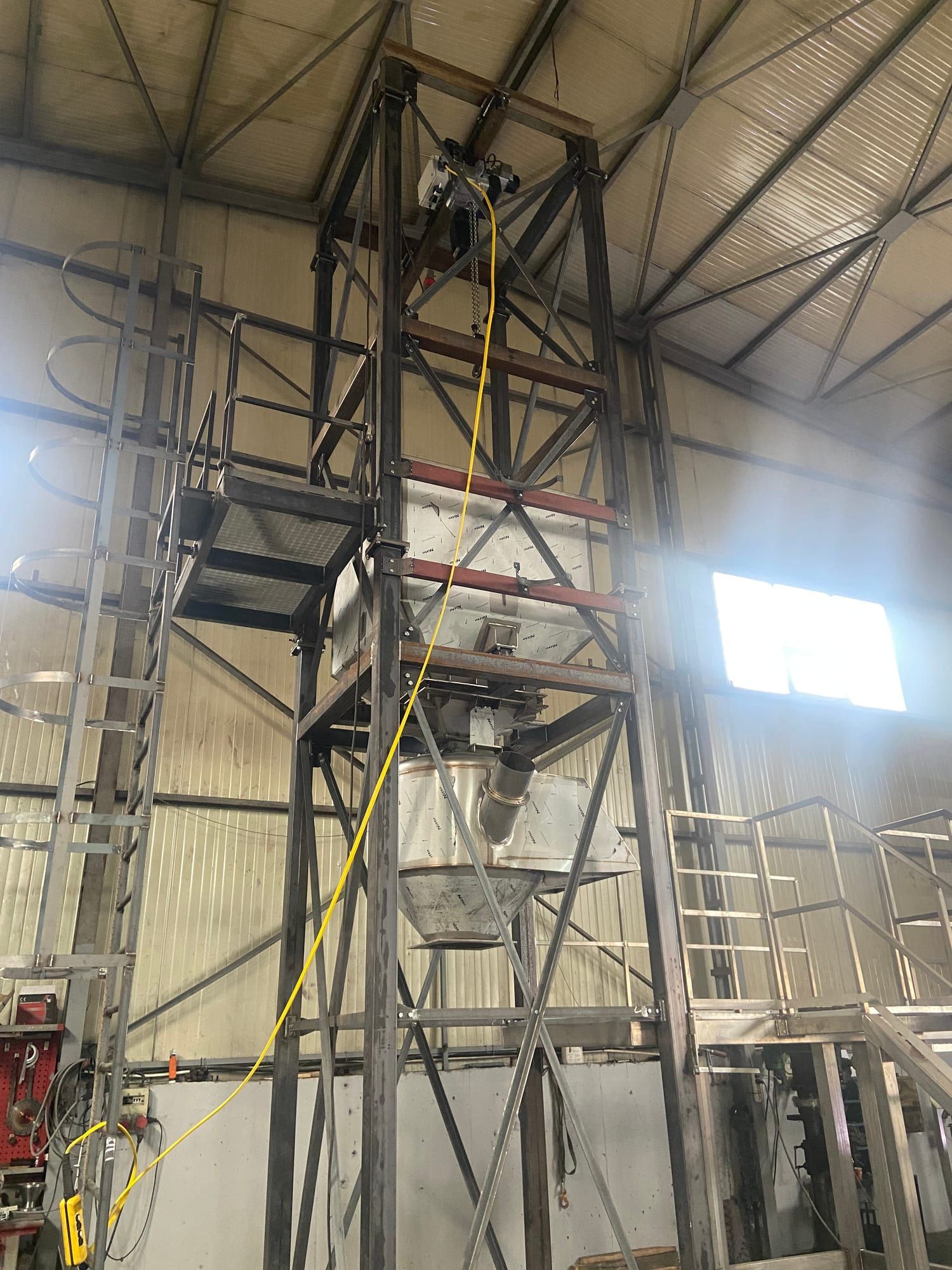 Hoher Stahlturm in der Werkstatt mit Kran oben sowie Plattform und Edelstahltrichter in der Mitte